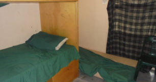 Image of double bunk beds, and a mattress on the floor by the window covered by a blanket at Broome Regional Prison