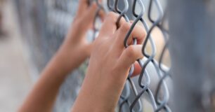 Image of a young persons hands holding onto a wire fence