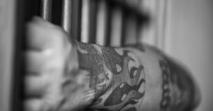 Image of a prisoners arm through bars in a cell