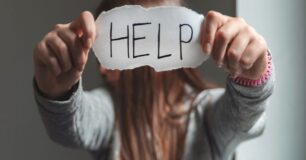 Image of a woman holding up a piece of paper with the word HELP written on it.