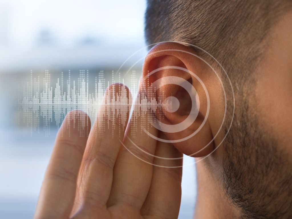 Image of a young man holding his ear trying to hear better.